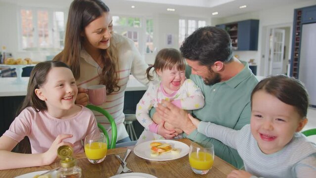 Family with Down Syndrome daughter sitting around table at home eating pancakes, fruit and syrup for breakfast - shot in slow motion