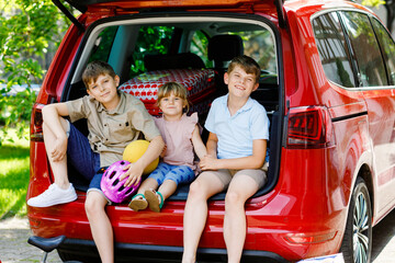 Three children, two boys and preschool girl sitting in car trunk before leaving for summer vacation...