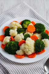 Mixed Organic Steamed Vegetables (Carrots, Broccoli and Cauliflower) on a Plate on a white wooden background, side view.