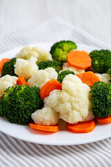 Mixed Organic Steamed Vegetables (Carrots, Broccoli and Cauliflower) on a Plate on a white wooden background, side view.