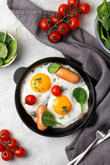 Frying Pan of fried eggs with sausages, spinach, tomatoes. Breakfast idea. Top view.