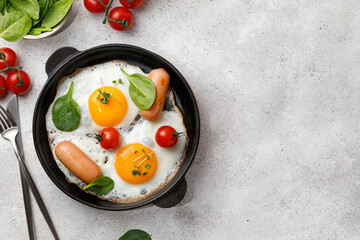 Fried eggs in a small pan with tomatoes, spinach, sausages. English breakfast, Top view, copy space. Keto, paleo breakfast