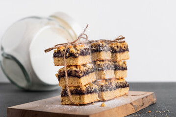 Cookies with currant jam are stacked and tied with twine and sprinkled with powdered sugar. On a wooden board. On a gray table. Glass jar in the background.