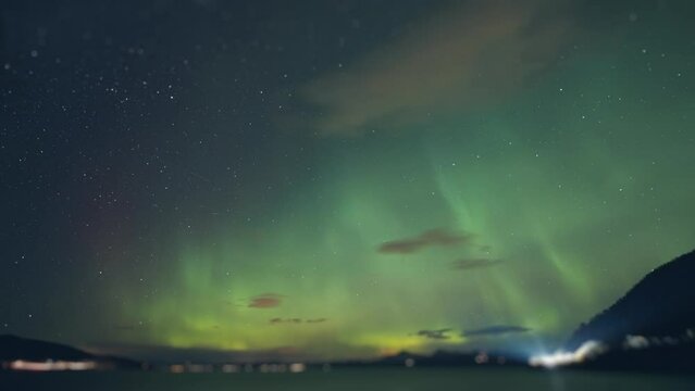 Northern lights above the fjord. Street and car lights flash in the background. Timelapse.