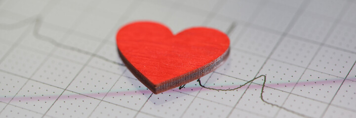 Toy red heart lying on paper with electrocardiogram closeup