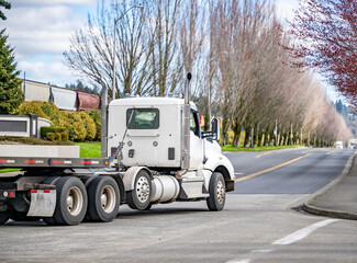 Powerful day cab big rig semi truck with flat bed semi trailer turning on the local road in industrial area running to warehouse