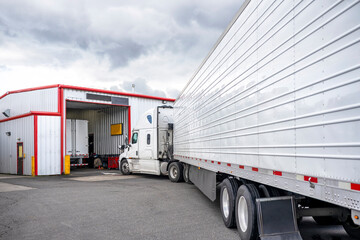 Professional white big rig semi truck with refrigerator semi trailer standing in line to truck repair and maintenance workshop