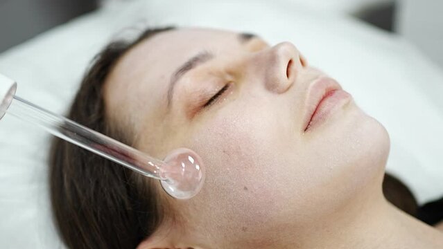 Beautician uses the darsonval device on the client's face. Professional skin care in the salon. The concept of cosmetology and rejuvenation.