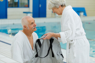 happy senior couple in bathrobe by resort pool - obrazy, fototapety, plakaty
