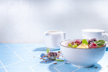 Summer breakfast healthy diet bowl with yogurt, granola, fresh fruit and berries, One portion with overnight fruity granola oats on sun-lighted tiled blue background copy space