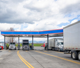 Truck drivers refuel tanks of different big rigs semi trucks at the truck stop gas station