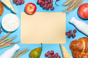 Happy Shavuot greeting card background with food Symbols of jewish Shavuot holiday - pomegranate, grapes, apple, sweet challah bread, wheat spikelets, milk, cheese, cottage cheese, on light blue backg