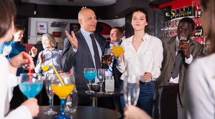 Smiling man enjoying conversation with young female colleague on corporate party in bar