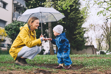 Young mother with her son walking in park in rain. Woman and little child explore nature around...
