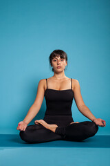 Fototapeta premium Personal trainer sitting on yoga mat in lotus position meditating during fitness workout. Athlete woman working at body posture practicing spiritual meditation. Concept of fitness exercise