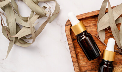 top view of Blank amber glass essential oil bottle with pipette on concrete background with eucalyptus leaves