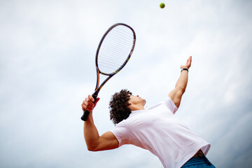 Young handsome tennis player with racket and ball prepares to serve at beginning of game or match.