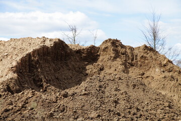 A pile of construction sand with traces of an excavator bucket on blue sky and dead bare trees background. Building construction and ecology