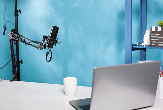 Professional microphone swivel boom arm stand in empty vlog broadcasting studio used for recording social media content. Audio live broadcast desk setup with digital mic and laptop computer.
