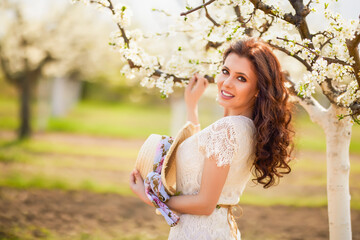 Portrait of a beautiful woman with long hair near flowering trees in spring.