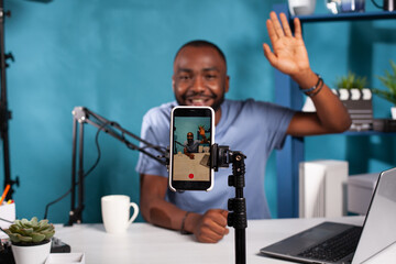 Closeup of live vlog setup with smarthone on stand filming content creator waving hand to followers...
