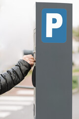 unrecognizable young woman paying in a parking meter