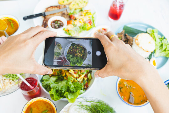 Woman's hand takes pictures of food on table with phone. Dinner or lunch raw vegan zucchini pasta with suace dipped avocado smartphone pictures for healthy vegan vegan social networking posts.