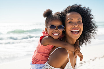 Happy young mother giving laughing daughter piggyback ride at beach