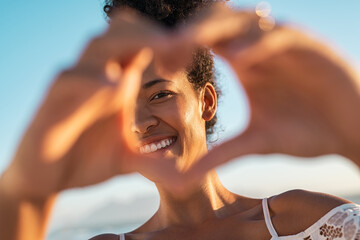 Black lovely woman making hand heart at beach during sunset