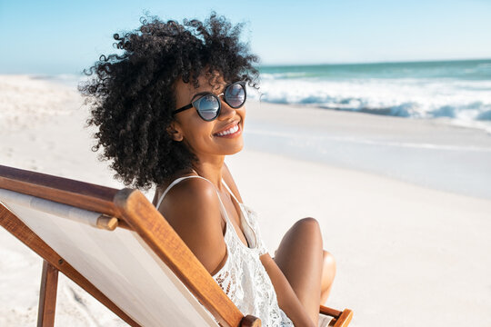 Happy smiling african woman sitting on deck chair at beach