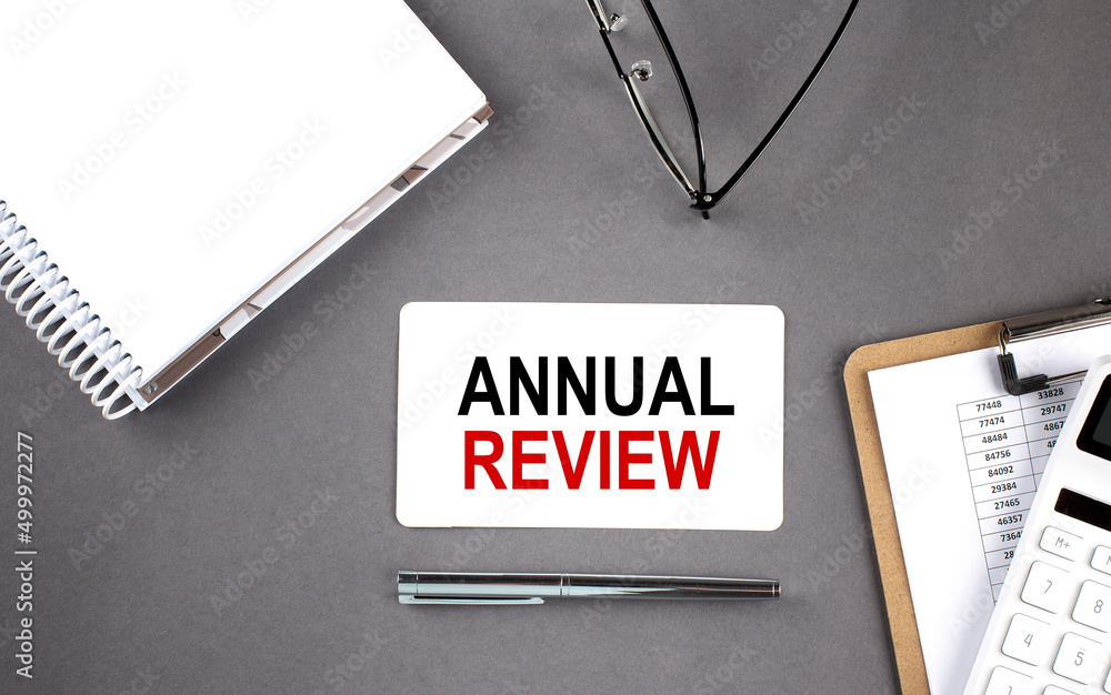 Poster annual review text written on the card with notebook and clipboard, grey background
