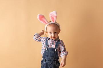 Obraz na płótnie Canvas Cute little boy with bunny ears on beige background. Happy Easter