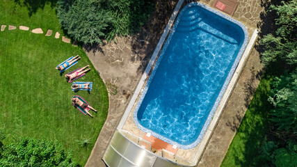 Happy family relaxing by swimming pool in summer garden, aerial drone view from above of parents...