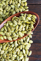 Pumpkin seeds in a wooden spoon on a wooden background. Healthy food. Scattered seeds of pumpkin. Vertical orientation