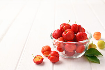 Acerola cherry in glass bowl on white wood.