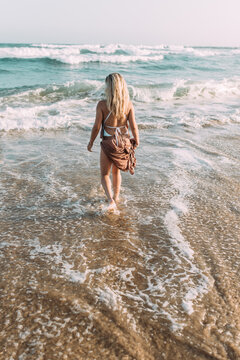 Junge blonde Frau mit langen Haaren am Strand im Wasser am Meer