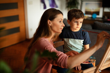 Mother and son painting at home. Little boy drawing with mom in living room..