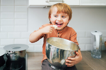 Cute little blond preschool kid boy baking cake in domestic kitchen, indoors. Laughing child ...