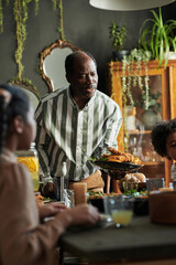 African mature man serving dish on dining table while having dinner with his family