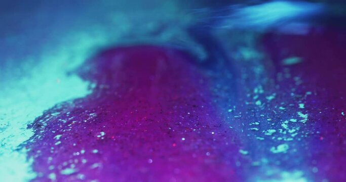 Glitter ink flow. Color fluid mix. Bokeh light. Defocused fluorescent purple pink blue shimmering particles paint motion abstract art background shot on RED Cinema camera.