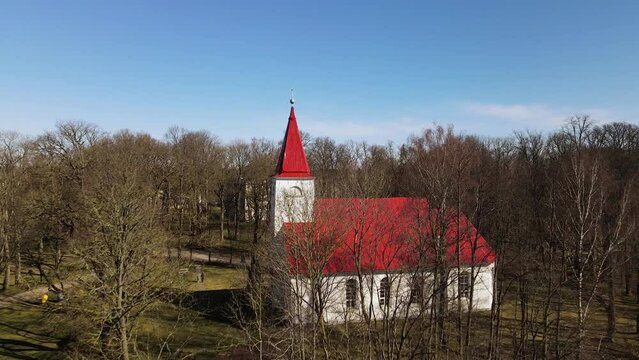 Aerial view of Lielvarde (Latvia) Lutheran church at the bank of Daugava river, white church with red roof through the leafless trees, sunny spring day, wide shot moving forward