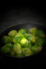 Brussels sprouts seasoned with sea salt in a black dish. On a stone background