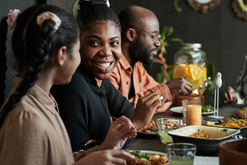 African happy woman talking to girl while sitting at dining table with members of her family