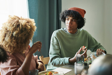 Teenage boy talking to his mother while they sitting at table and having dinner at home