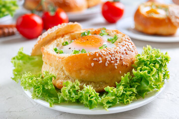 Breakfast eggs. Baked buns stuffed with eggs and bacon and fresh herbs on plates on a light background.  Close up
