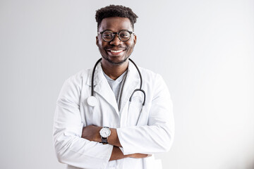 Fototapeta premium Portrait of happy african doctor at private clinic. Happy african american male nurse. Friendly african male therapist posing over gray background. Medical concept of young male doctor in white coat