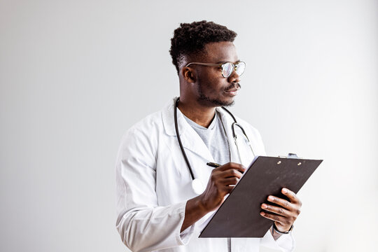 Portrait Of Smiling Black Male Doctor With Stethoscope On White Background. Young Happy Black Medical Doctor Holding Medical Chart Over White Studio Background, Copy Space..