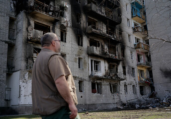 A man stands in front of the facade of a destroyed house during military operations in Ukarin