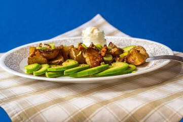 Avocado, baked potato with onion and garlic on plate, checkered table-cloth on blue