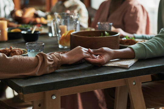 Close-up of family sitting at dining table holding hands and praying before dinner